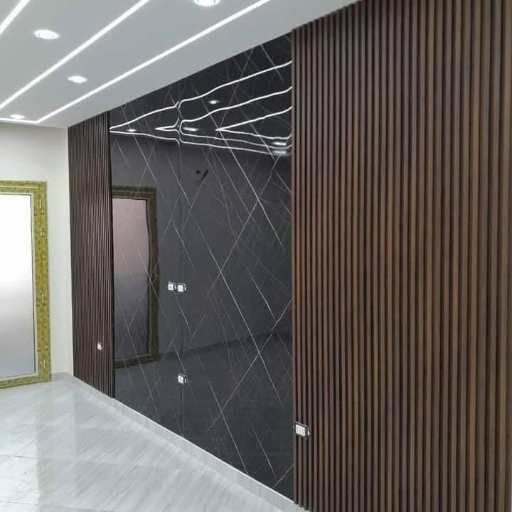 تصميم داخلي مودرن يدمج بين ألواح بديل الرخام الأبيض ذو العروق الرمادية وتكسيات بديل الخشب البني مع إضاءة ليد خلف الشاشة بالدمام - تنفيذ ديكورات الشرقية.