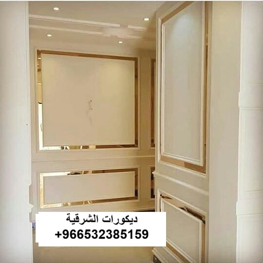 حائط مجلس رجال فخم يدمج بين بانوهات الفوم الأبيض المطفي وشرائح الاستيل الذهبي اللامع بتنسيق نيوكلاسيك راقٍ في الدمام - تنفيذ مؤسسة ديكورات الشرقية.